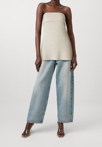 Top senza spalline beige a coste con un corpo aderente, abbinato a jeans a gamba larga blu chiaro e sandali con tacco trasparente.