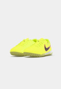 Par de zapatillas deportivas Nike de color amarillo brillante con logotipos de swoosh en negro y rojo, suelas texturizadas y cordones sobre un fondo blanco liso.