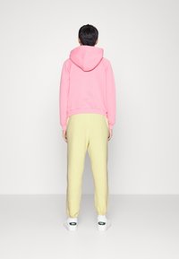 Rosa bomullshoodie med huva, i kombination med gula sweatpants. Outfiten har en avslappnad passform, ribbade ärmmuddar och vita sneakers.