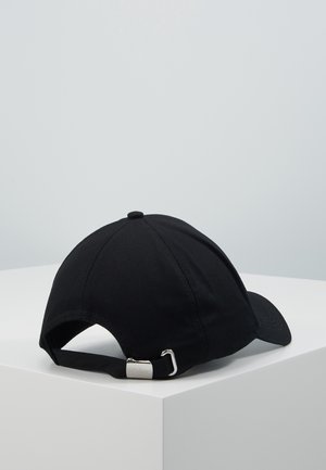 Sort justerbar baseballkasket med metal spænde på hvid pedestal mod lysegrå baggrund.