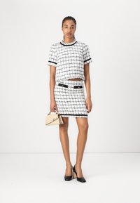 Two-piece outfit featuring a white and black tweed top with short sleeves and a matching skirt. Black accents and buttons are present.