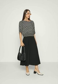 Saia preta plissada combinada com uma blusa de manga curta com padrão em preto e cinza, acompanhada de sapatos de salto bejes e uma mala preta.
