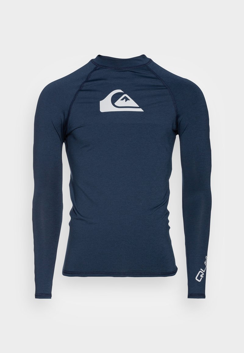 Rash guard de manga larga en color navy hecho de material elástico. Presenta un logo blanco en el pecho y detalles en el texto en la manga. Textura suave.