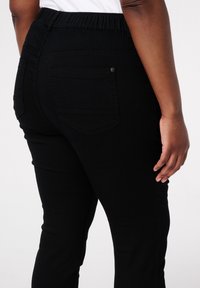 Pantalons en denim noir avec une taille élastique haute, dotés de deux poches arrière et de jambes ajustées qui s'affinent légèrement vers la cheville.