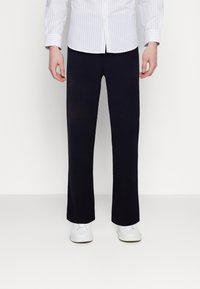 Navy blue pants in a straight-cut design. Made of a smooth fabric, they feature an elastic waistband and are paired with white sneakers.