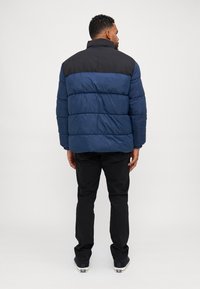 Doudoune avec une partie inférieure bleu marine et une partie supérieure noire. Motif matelassé horizontal, col haut et manches longues. Portée avec un pantalon noir.