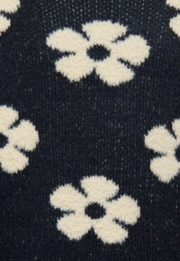 Tejido de punto azul marino con una textura suave que presenta grandes patrones florales blancos, cada uno con un punto central, creando un contraste audaz.