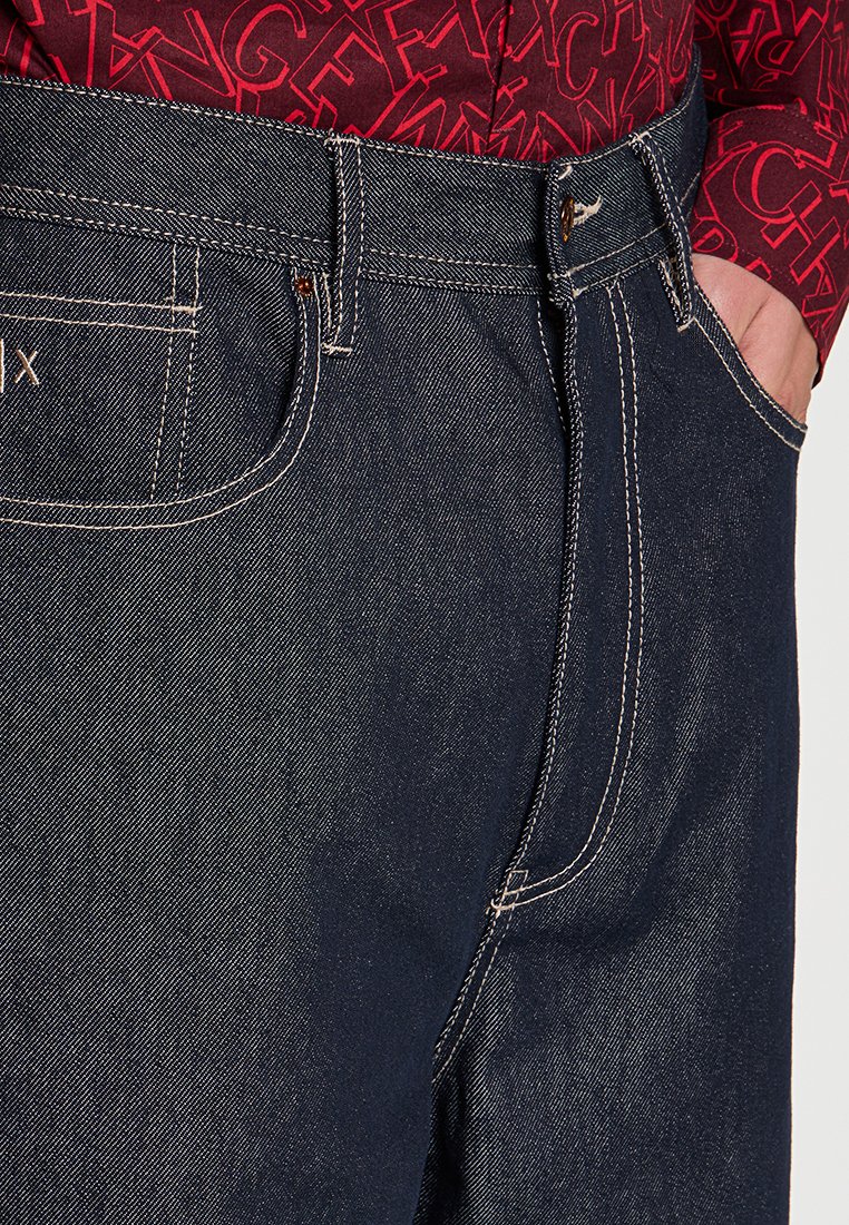 Dunkelblaue Jeans aus Denim mit heller Naht, ausgestattet mit Fronttaschen und einem klassischen Schnitt. Das Material wirkt robust und hat eine glatte Textur.