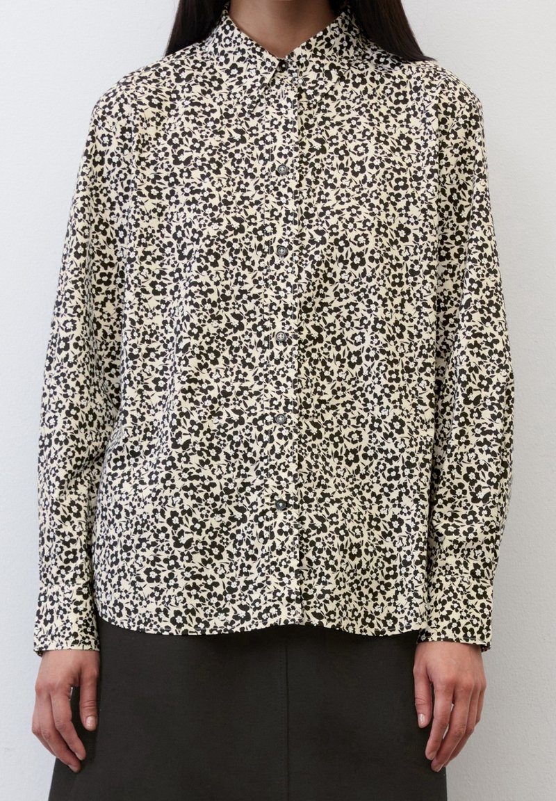 Camicia a maniche lunghe color crema con motivo floreale nero, chiusura con bottoni, colletto e vestibilità rilassata. Tessuto morbido con una texture liscia.