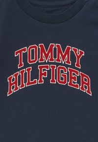 Námořnické tričko z bavlny s velkým červeným nápisem "TOMMY HILFIGER" v obloukovém designu. Kulatý výstřih a měkká textilie.