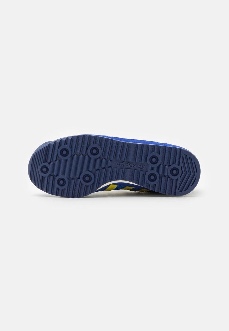 Suela de goma navy con surcos texturizados y dibujos circulares, con acentos en amarillo y blanco. Logotipo grabado en el lateral.