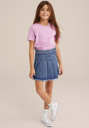 Camiseta de algodón rosa con un pequeño logo, combinada con una falda de mezclilla azul con pliegues y zapatillas altas blancas con acentos coloridos.
