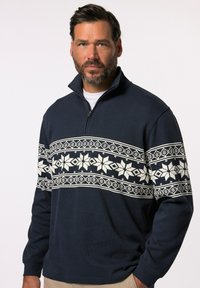 Námořnický svetr s vysokým límcem, na jehož hrudi je bílý vzor sněhové vločky, se žebrovanými manžetami a detailem s polozipem na přední straně.