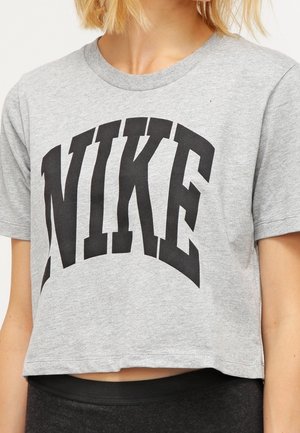 T-shirt gris court en coton avec un col rond. Présente une grande inscription noire "NIKE" en lettres majuscules et grasses sur le devant.