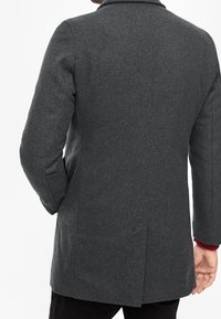 Cappotto in misto lana carbone con colletto a revers, apertura singola sul retro e maniche lunghe. Finitura testurizzata, vestibilità sartoriale, senza hardware visibile.