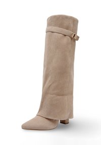 Botte beige au-dessus du genou en daim doux. Présente un bout pointu, un talon bloc et une sangle avec une boucle métallique en haut.