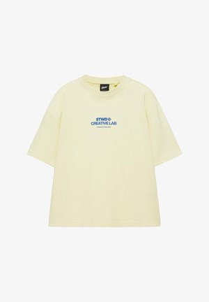 Halvány sárga, oversized rövid ujjú póló kék "STWD CREATIVE LAB CREATING SINCE 1991" felirattal a mellkas közepén.