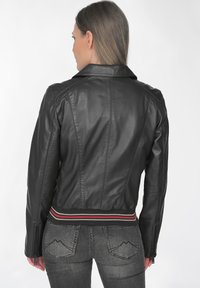 Schwarze Lederjacke mit strukturiertem Design, ausgestattet mit einem gerippten Taillenbund mit roten und weißen Streifen sowie mit Reißverschluss versehenen Bündchen.