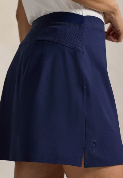 Ναυτικό μπλε αθλητική φούστα με ομαλή υφή, διάτρητη μέση, λεπτομέρεια με πλαϊνή σχισμή και κεντημένο λογότυπο στο τελείωμα.