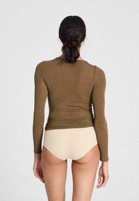 Maglia a maniche lunghe color marrone realizzata in un tessuto testurizzato, abbinata a slip beige chiaro, vista da dietro su uno sfondo neutro.