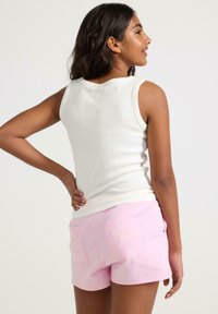 Hvid ribbet tanktop kombineret med lyserøde shorts med lommeudsmykninger og dragsnor, der viser et afslappet, tætsiddende design.