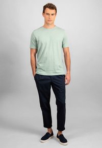 Green short-sleeve t-shirt with a round neckline, paired with navy tapered pants and dark slip-on shoes, set against a neutral background.