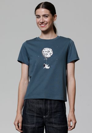 T-shirt en coton bleu-vert à manches courtes, avec un graphique d'astronaute blanc tenant un ballon en forme d'une lune cratérisée.