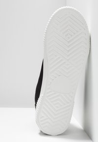 Sort ruskindssneakers med hvid gummisål, der har et tekstureret zigzag-mønster for bedre greb. Hælen er helt hvid med en afrundet detalje.