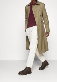 Khaki trench coat with a double-breasted design, maroon sweater, white trousers, and brown chelsea boots. Smooth, structured fabric.
