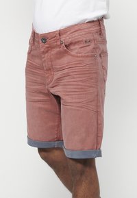 Shorts en denim rouge avec des poignets gris retroussés, présentant un design à cinq poches et des détails de couture visibles. Fermeture par bouton à l'avant.