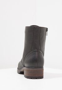 Botín negro de cuero hasta el tobillo con punta redondeada, cremallera lateral y tacón de bloque de madera. El diseño presenta un detalle de costura en los laterales.
