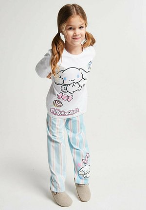 Young girl with blonde pigtails wearing white shirt and blue striped pants featuring Cinnamoroll character and candy illustrations.