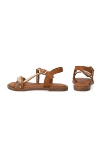 Braune Leder-Sandalen mit einem schmalen, goldakzentuierten Riemen und einem geknoteten Detail an der Oberseite. Flache Sohle und verstellbare Knöchel-Schnalle.