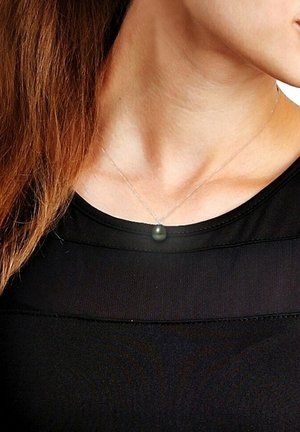 Collier en argent arborant un pendentif rond gris-vert, porté sur une chemise noire, mettant en évidence un design simple et élégant.