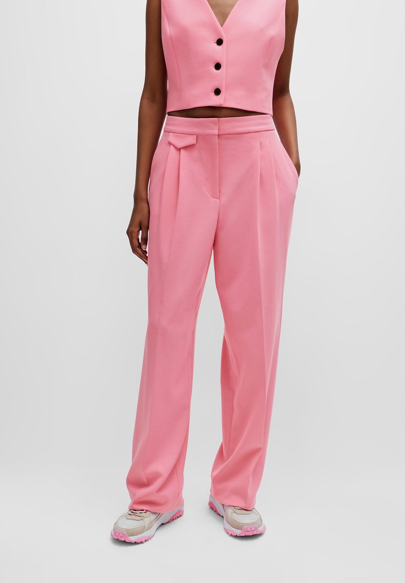 Lyserød cropped top med sorte knapper, kombineret med lyserøde brede bukser med en sidelomme og plisseringer. Tekstureret stof. Afslappet fodtøj.