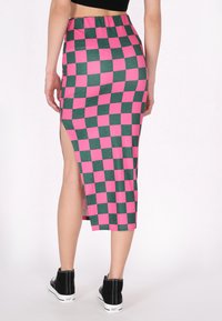 Hosszú, testhezálló szoknya zöld és rózsaszín sakktáblaszerű mintával, oldalhasítékkal és rugalmas derékkal. Fekete bokacsizmával párosítva.