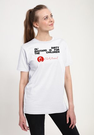 Donna con lunghi capelli castani, in camicia bianca e pantaloni neri, guarda in alto, testo sulla camicia: "Ol' Dirty Bastard is for the children" con logo rosso.