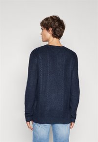 Pull en maille bleu marine avec un motif en câble texturé, col rond et manches longues. Coupe décontractée, tissu doux et poignets côtelés.