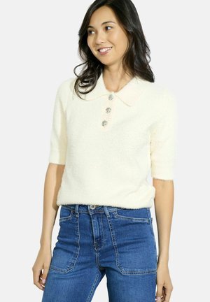 Fluffy cream sweater with a flat collar, short sleeves, and three decorative buttons. Worn with high-waisted blue jeans.