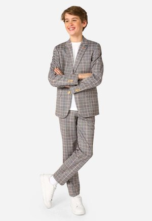 Blazer à carreaux gris et pantalon assorti, avec des accents jaunes et bleus. Porté avec un t-shirt blanc et des baskets blanches.