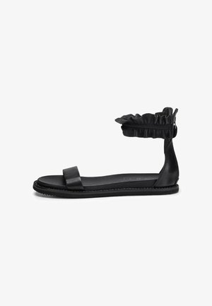 Sandal nero piatto con una singola fascetta larga sopra il piede e un polsino arricciato alla caviglia. Materiale in pelle liscia con suola piatta e bordi testurizzati.