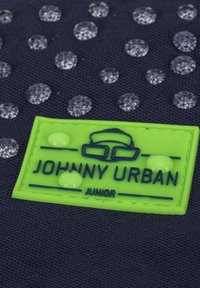 Tengerész kék szövet, texturált felülettel, amelyen tiszta vízcseppek és egy élénk zöld gumicímke található "JOHNNY URBAN" és "JUNIOR" felirattal.