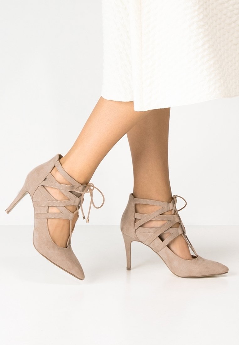 Chaussures à talons hauts en daim beige avec un bout ouvert et un design de brides croisées complexes, présentant un bout pointu et un talon aiguille fin.