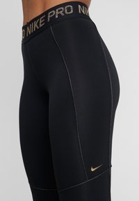 Czarne legginsy Nike Pro z złotym logo. Gładki, elastyczny materiał z kontrastowymi szwami. Szeroki pas ze znakowaniem.