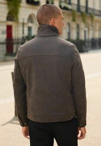 Braune Lederjacke mit erhöhtem Kragen, sichtbaren Nähten und geknöpften Manschetten. Mit einer taillierten Silhouette und glatter Textur gestaltet.