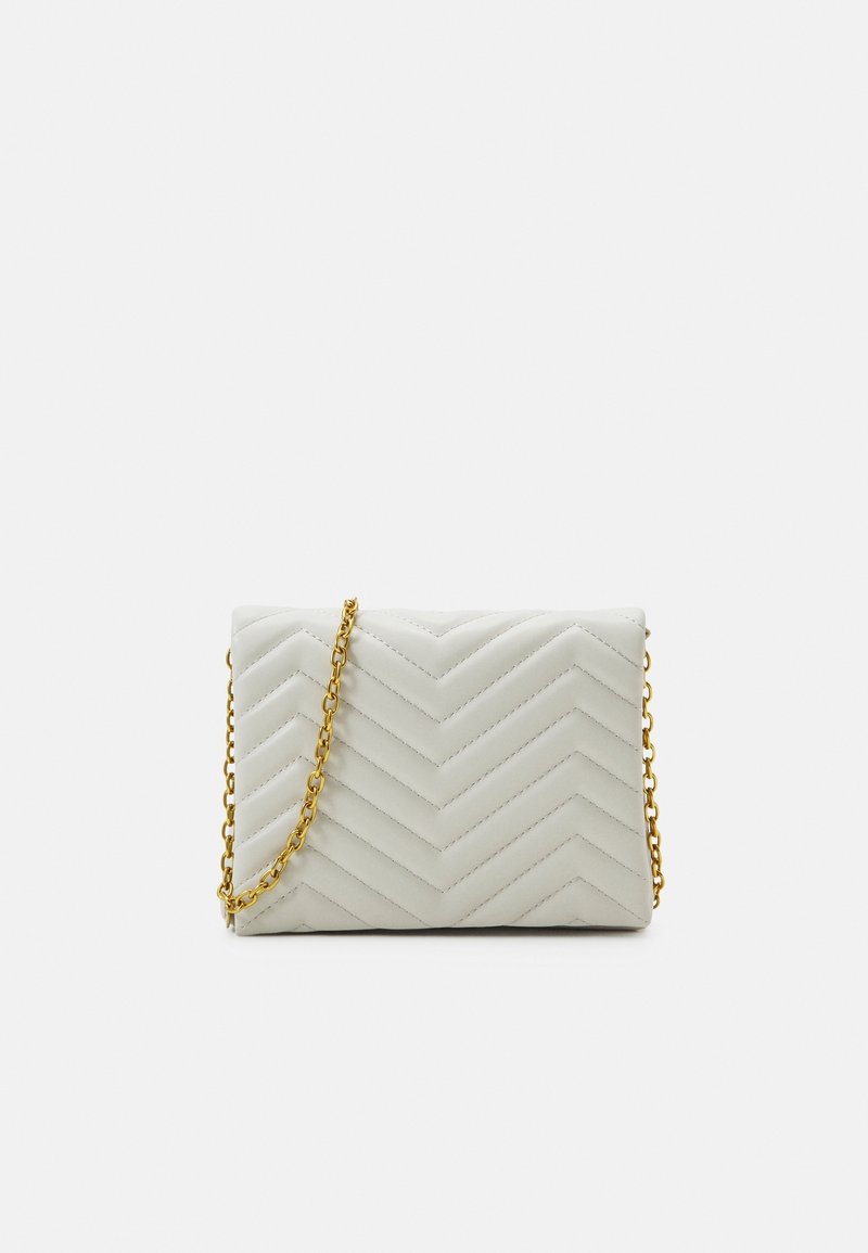 Petit sac à main blanc matelassé avec motif de points en chevron et bandoulière chaîne dorée sur fond blanc.