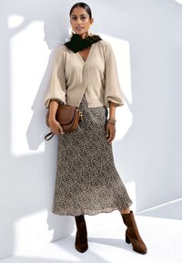 Beige gestrickte Strickjacke über einem midi-Kleid mit Leopardenmuster, kombiniert mit braunen Wildleder-Stiefeletten und einer sandfarbenen Umhängetasche.