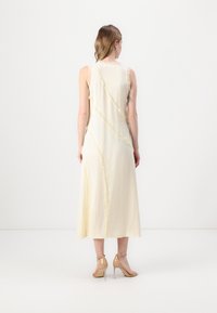 Rochie galbenă, lungă, fără mâneci, cu cusături texturate și desfăcute, o siluetă fluidă și un guler rotund. Purtați-o cu sandale cu toc de culoare neutră.