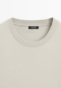 T-shirt beige en coton à col ras-du-cou avec col en côte, affichant l'étiquette "Massimo Dutti Made in Portugal" à l'intérieur de l'encolure.