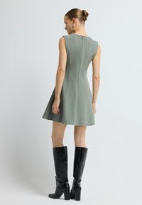 Bezramenn�é zelené šaty s rozšířenou sukní, se zadním zipem a jemným švem, doplněné černými koženými botami s vzorem krokodýlí kůže do výšky kolen.